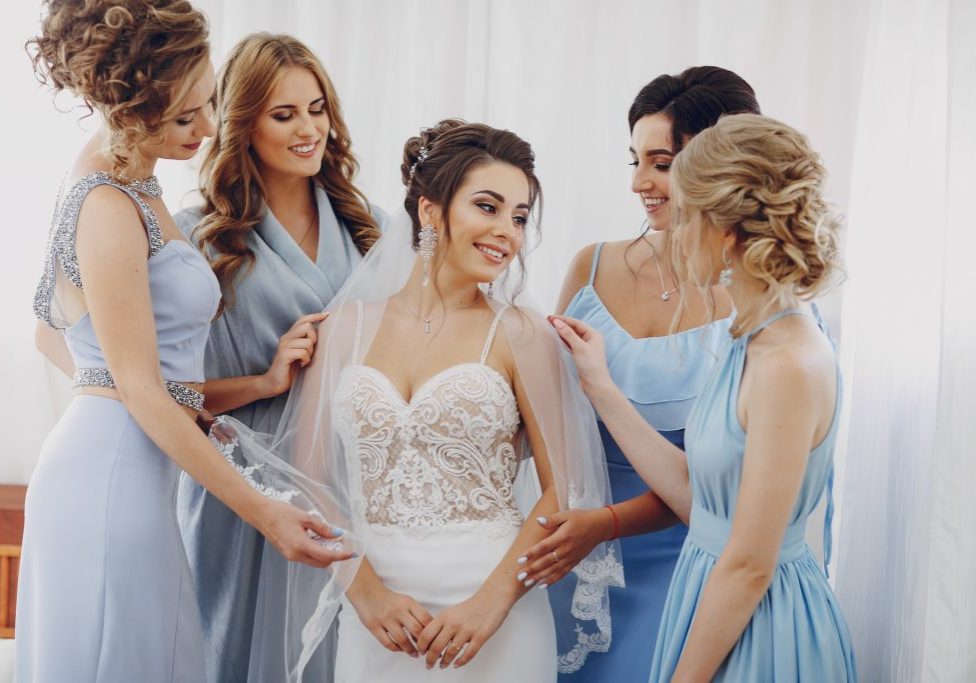 elegant and stylish bride along with her four girlfriends in blue dresses standing in a room
